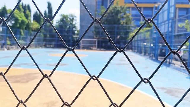 Close up of a metal chain link fence with a blurred outdoor sports court background