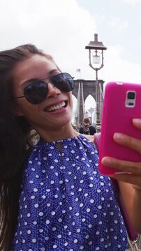 Happy woman using phone texting walking on Brooklyn bridge, New York city for social media. Tourist doing summer travel in Manhattan, USA. Vertical Video. Video is unretouched and model without makeup
