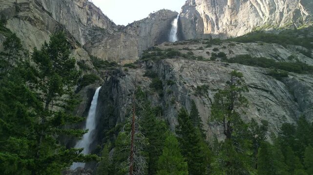Aerial shot of Yosemite Valley featuring cascading waterfall surrounded by granite cliffs, dense forest, and dramatic mountain landscape in California&rsquo;s Sierra Nevada.