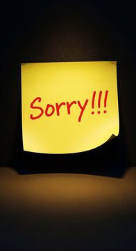 Yellow sticky note with apology message on dark desk.