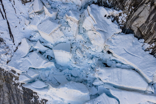 Aerial View of Broken Glacier Ice and Crevasses Against Rocky Cliffs in British Columbia, Canada