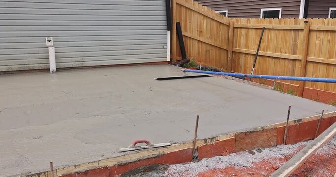 Workers prepare pour concrete for new slab foundation in backyard near garage