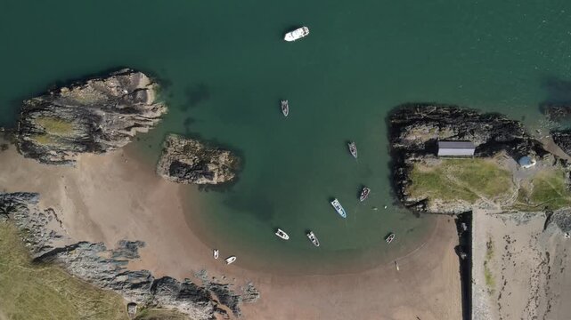 Aerial view of small boats anchored in the turquoise waters of a sandy cove at Ynys Llanddwyn on the coast of Wales, United Kingdom.