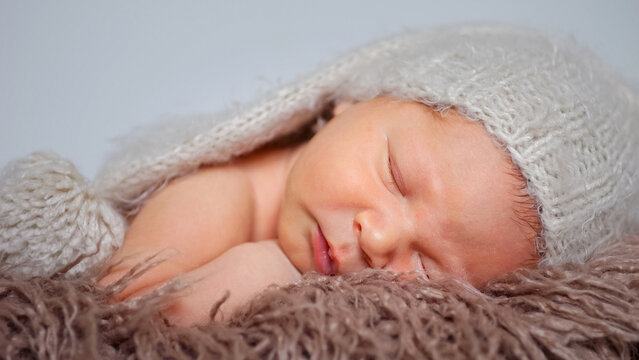 Newborn baby boy sleeping calmly on a fluffy brown blanket, wearing a light grey knitted hat, portraying innocence, comfort, and the serenity of early slumber
