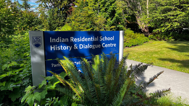 Blue UBC sign for the Indian Residential School History and Dialogue Centre, set among ferns and lush greenery on the University of British Columbia campus.