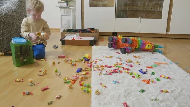 Boy unwrapping a candy hamburger next to a broken birthday pi&ntilde;ata with spilled sweets
