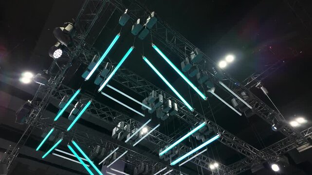 A striking overhead display of suspended LED light bars and stage lighting equipment creates a futuristic geometric pattern. 