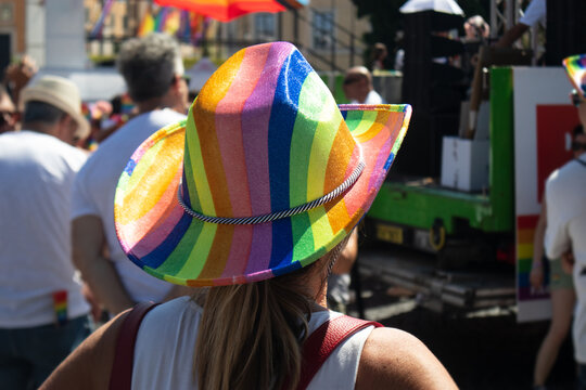 Primo piano ravvicinato dello schienale di una persona che indossa un cappello da cowboy con i colori dell'arcobaleno in mezzo alla folla durante una sfilata del Pride, simbolo di gioia e orgoglio LGB