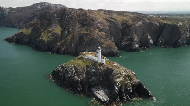 Aerial view of South Stack Lighthouse perched on a rocky island against steep cliffs and the Irish Sea in Holyhead, Wales, United Kingdom.