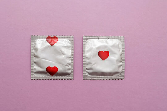 Two condom packets decorated with red hearts on a pastel pink background. Minimal flat lay composition representing safe sex, love, romance, Valentine's Day, sexual health and relationship protection.