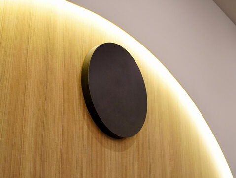Modern minimalist interior wall decoration featuring a blank black circular sign mounted on a textured wooden panel with warm hidden LED cove lighting