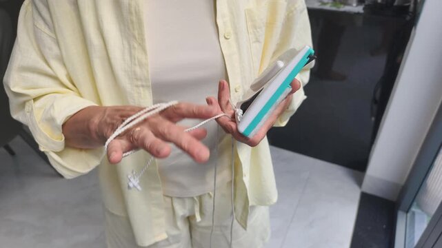 Woman fastens safety rope around wrist before washing glass. Smart preparation using strong safety rope prevents magnetic cleaner from falling down, ensuring secure and professional window care.