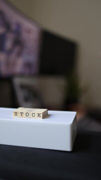 Vertical screen Wooden blocks spelling stock on a white surface while a woman browses creative content in the background representing stock footage photography and digital media licensing
