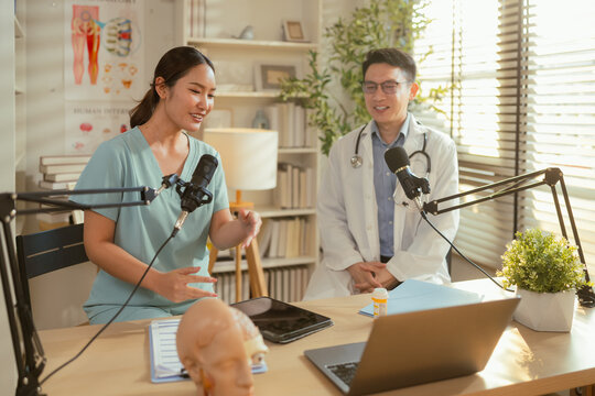 Asian doctor and nurse recording medical podcast with microphones in studio office, healthcare professionals discussing health topics with anatomy models and laptop, medical broadcasting content, copy