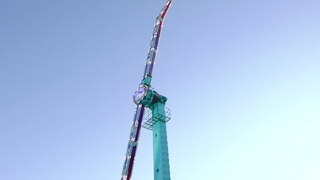 Colorful illuminated pendulum ride swings high against a clear evening sky, with riders suspended in seats during a thrilling fairground attraction.