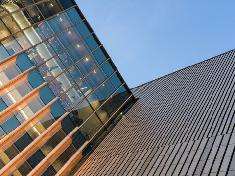 Modern glass building reflecting sunset light next to metallic facade against sky