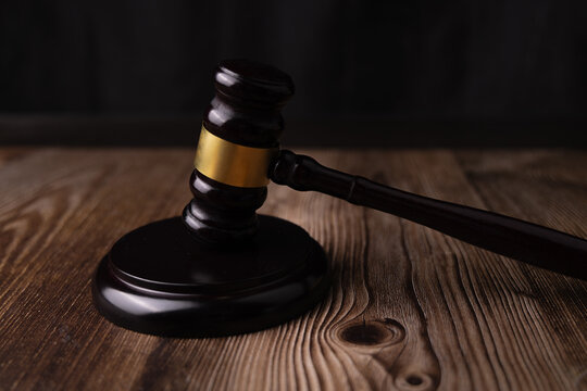 Angled eye level look of a mahogany judge gavel sitting on its official sound block element over a dark polished wood background