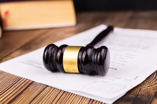 Front angle layout of a mahogany judge gavel resting on official case papers and legal documents over a dark wood desktop surface