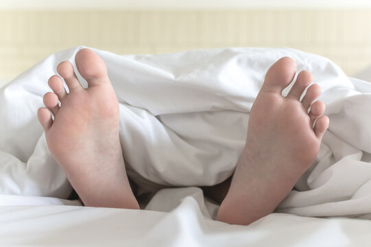 World sleep day, sleeping comfort, health relaxation and bedtime insomnia concept with young girl&rsquo;s bare foot laying lazy on bed resting in comfy hotel bedroom on white bed sheet