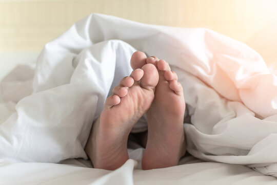 World sleep day, sleeping comfort, health relaxation and bedtime insomnia concept with young girl&rsquo;s bare foot laying lazy on bed resting in comfy hotel bedroom on white bed sheet