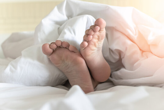 World sleep day, sleeping comfort, health relaxation and bedtime insomnia concept with young girl&rsquo;s bare foot laying lazy on bed resting in comfy hotel bedroom on white bed sheet
