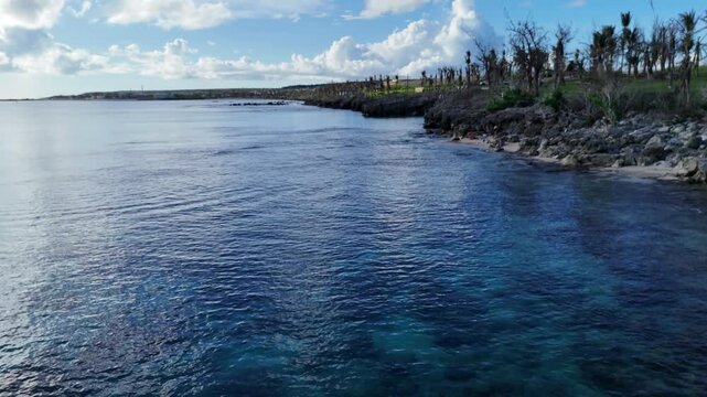 Aerial view of Taga Beach with clear turquoise water and rocky coastline under a blue sky in San Jose, Tinian, Northern Mariana Islands.