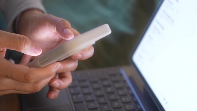Person using smartphone beside laptop while reviewing digital information, Business documents online. Paperless workflow, Verification process, rRemote work and Digital Transformation concept