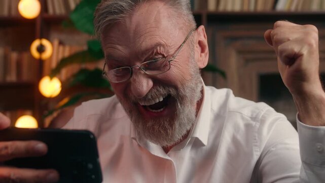 Carefree Caucasian old retirement business man using mobile phone winning watching sport championship rejoicing winning senior mature businessman male win with smartphone achievement at office table