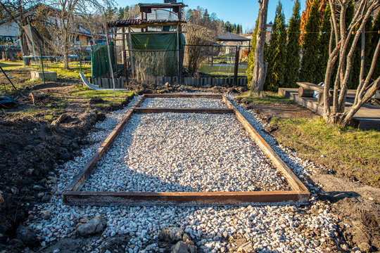 Rectangular foundation with rusted steel angles holds white crushed stone in a backyard workshop, late afternoon light casts long shadows on compacted aggregate.