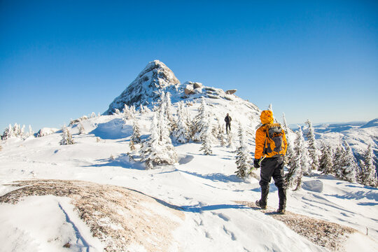 Two hikers trekking through deep snow towards a mountain