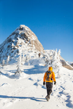 Person in yellow jacket hikes up snowy mountain trail