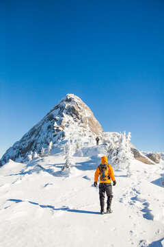 Hiker in orange jacket walks toward snowy summit