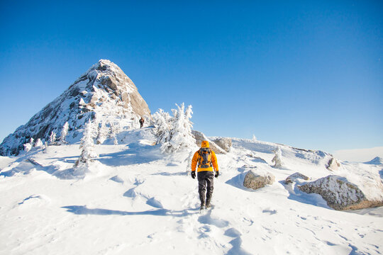 Man hikes through snow toward a mountain summit