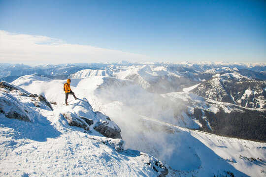 Hiker on snowy peak overlooking mountain range
