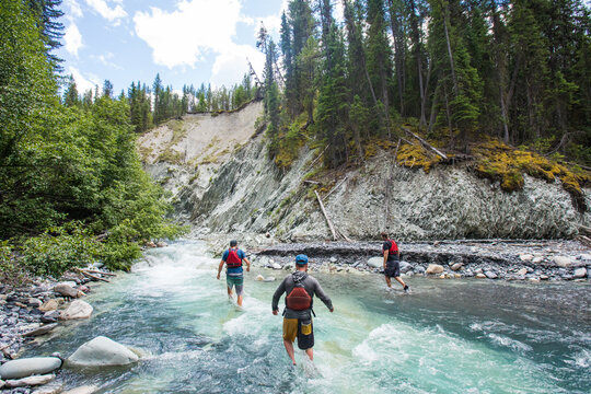 Three male friends hiking together through a mountain river