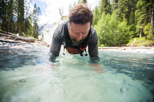Bearded man leaning over a shallow creek