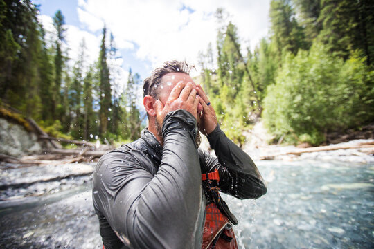 Wet man washing his face in a forest river