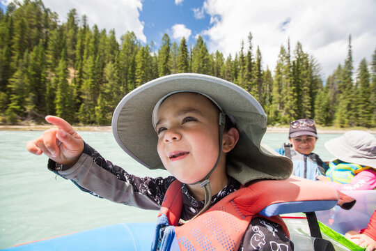 Young boy in sun hat points from a raft on a river