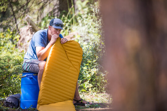 Man inflates a yellow sleeping pad while camping