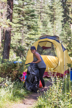 Smiling woman packs her backpack at a sunny campsite