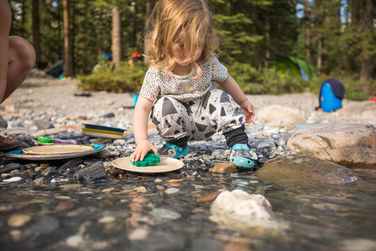 Toddler washing camping dishes in a clear stream