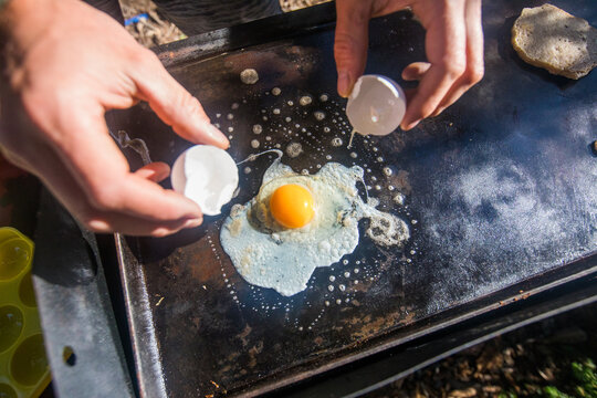 Hands cracking an egg onto a hot griddle outside