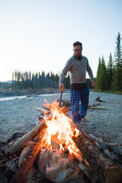Man with hatchet tending campfire at dusk