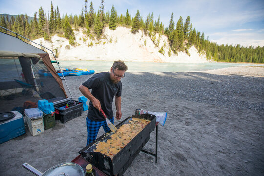 Man cooking a large breakfast on a griddle at riverside campsite