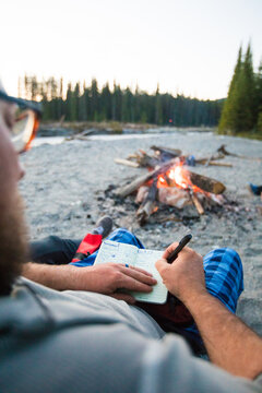 Man journaling in a notebook by a campfire