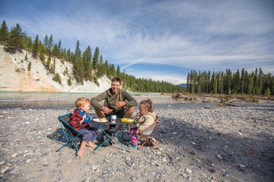 Father and two young children enjoy riverside picnic