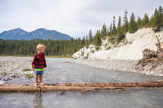 Young boy balancing on a log over a mountain river