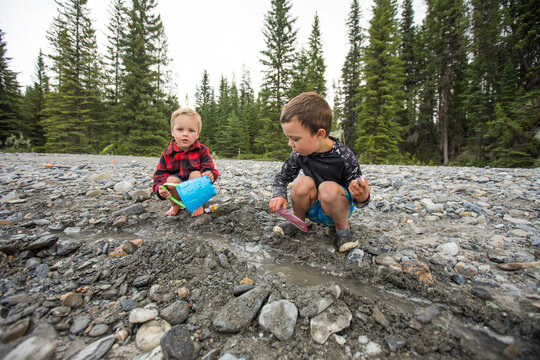Two young brothers play in a muddy riverbed