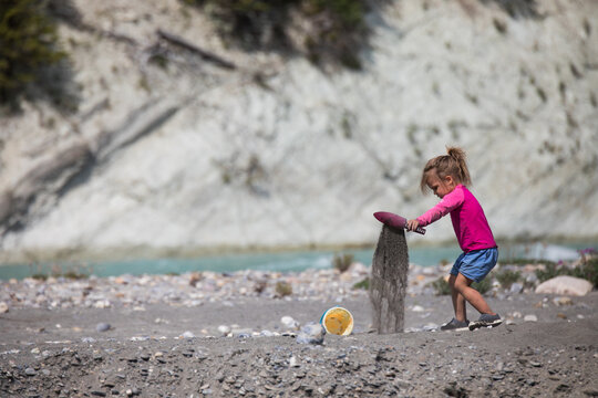 Young girl pours sand from a toy shovel by a river
