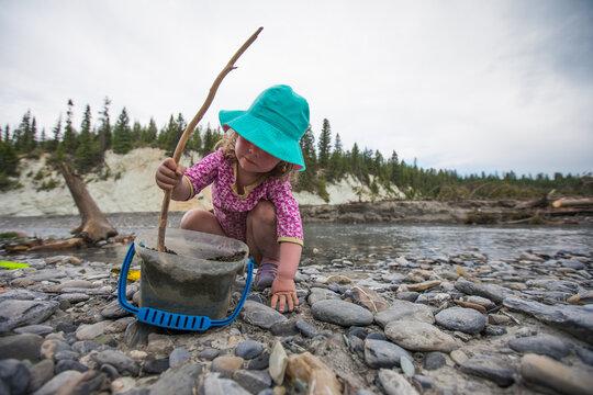Little girl plays with bucket on a rocky riverbank